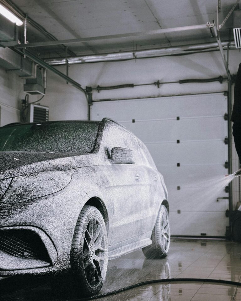 A luxury car gets foam washed in a modern garage with overhead lighting.