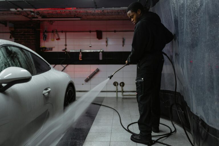 African American man cleaning a white car with a pressure hose in an indoor garage setting.