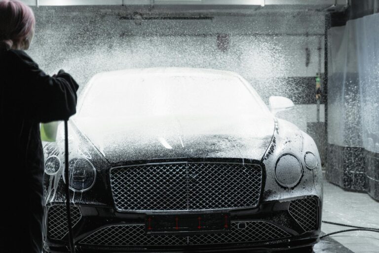 Black luxury car receiving a foamy wash in an indoor car wash service.