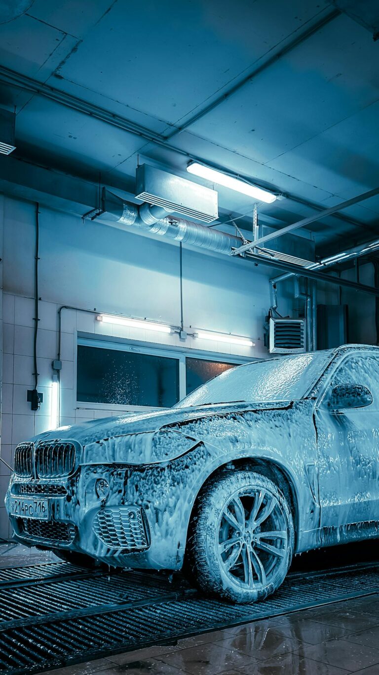 Luxury SUV covered in foam inside a modern car wash station enhanced by blue lighting.