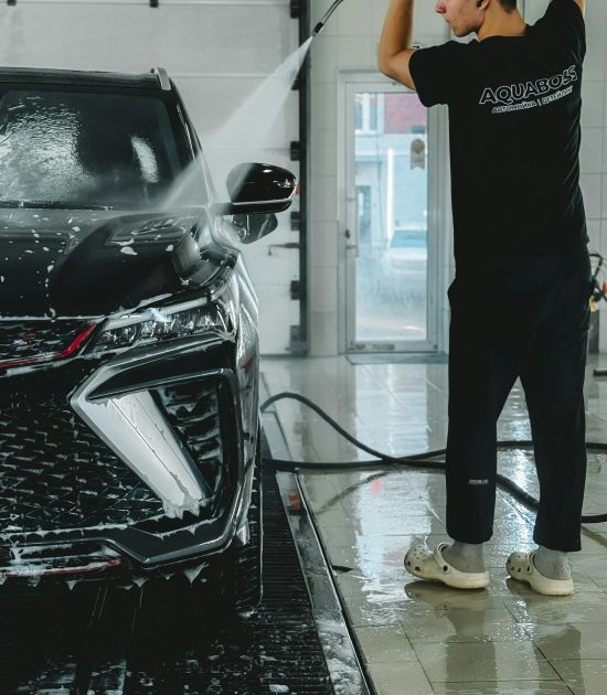 Young man using high-pressure water to clean a luxury car indoors.